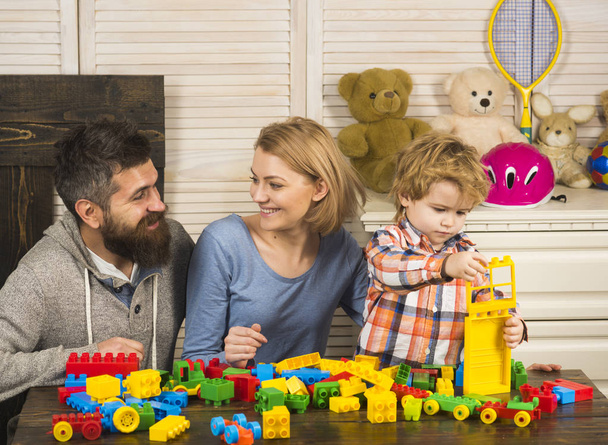 Parents with happy faces and kid makes brick constructions. - Foto, Bild