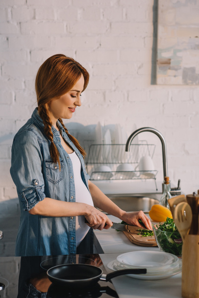 side view of attractive pregnant woman preparing salad at kitchen - Foto, Imagen