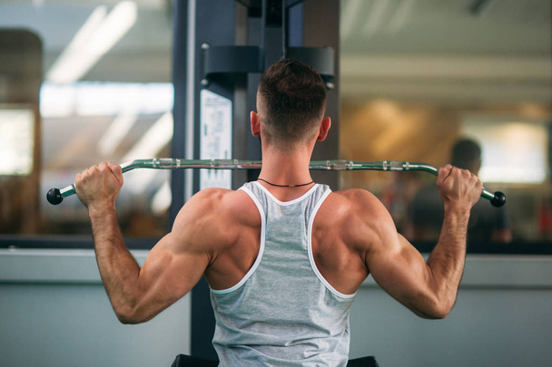 Un joven atleta entrena en el gimnasio. Muestra los músculos de la espalda y el pecho
 - Foto, Imagen