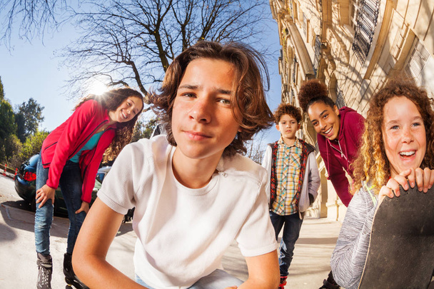Tizenéves fiúk és lányok, gördeszka és görkorcsolya ül össze a járdán közeli portréja - Fotó, kép