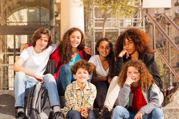 Big group of multiethnic teenage boys and girls sitting together outdoors on staircase at sunny day - Foto, Imagem
