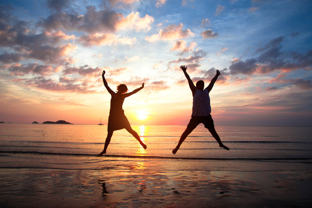 concept van de langverwachte vakantie: jong koppel in een sprong op de zee strand bij zonsondergang. - Foto, afbeelding