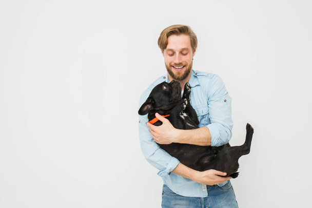 young and beautiful man holding his dog in his arms with love and playing with him, against a white background - Фото, зображення