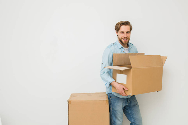 a young blonde man, carrying some cardboard boxes, delivery man, or a guy who moves things to another home on a white background, looking to camera - Фото, зображення