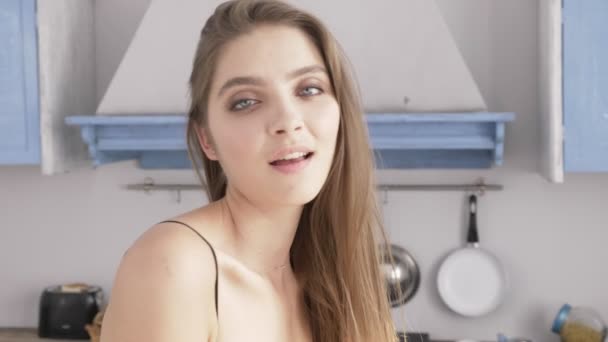 Portrait of a young sexy caucasian woman in black lingerie looking at the camera, kitchen in the background, close up 50 fps - Metraje, vídeo