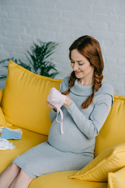 attractive pregnant woman looking at baby hat in living room - Photo, Image
