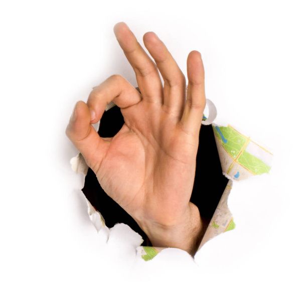 Nahaufnahme einer weiblichen Hand, die aus einem Loch in einem Papier kommt, Okay-Zeichen, isoliert auf weiß - Foto, Bild