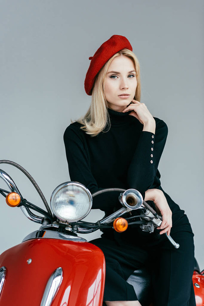 Fashionable blonde girl leaning on vintage scooter isolated on grey - Foto, Bild