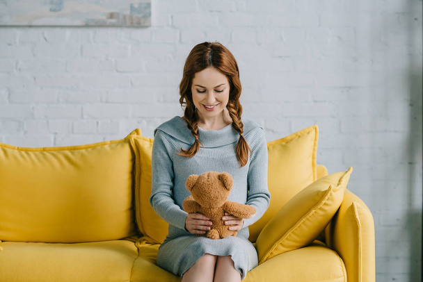 beautiful pregnant woman sitting with teddy bear in living room - Foto, Imagem