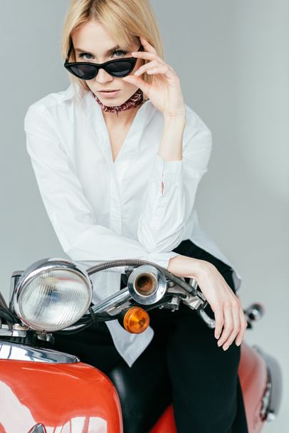 Stylish pretty woman in white shirt posing on red scooter isolated on grey - Zdjęcie, obraz