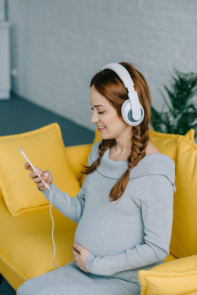 χαρούμενη έγκυος γυναίκα, να ακούτε μουσική στο σαλόνι - Φωτογραφία, εικόνα