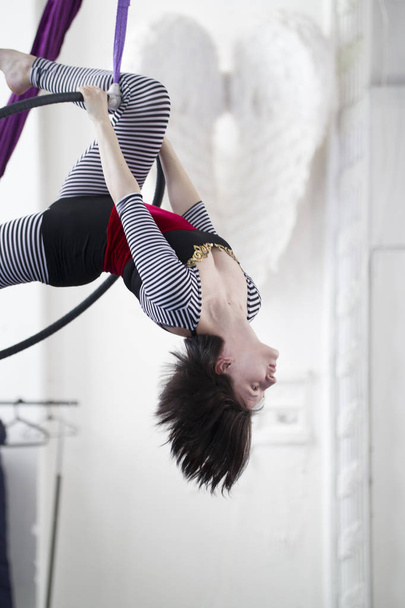 Гибкая женщина-гимнастка висит вверх ногами на воздушном обруче
 - Фото, изображение