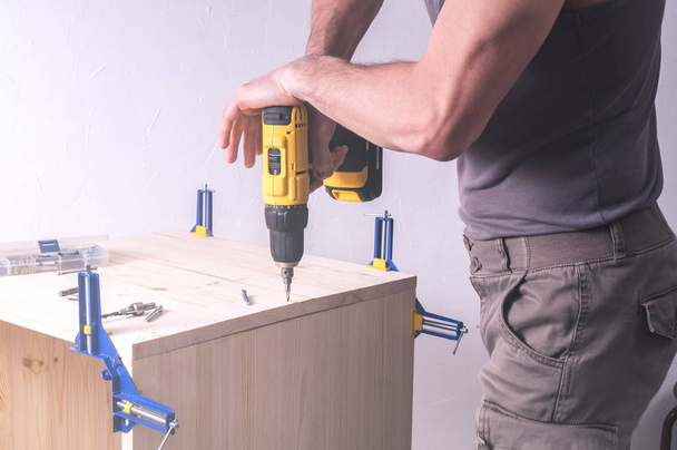 Men's work: A man works with a screwdriver. Assembling of cabinet furniture made of wood. - Foto, afbeelding