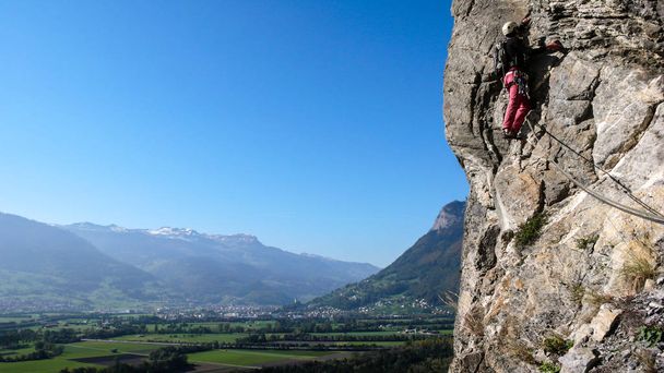 male rock climber lead climbing a steep rock route in the Alps with a great view of the Rhine Valley behind him - Фото, изображение