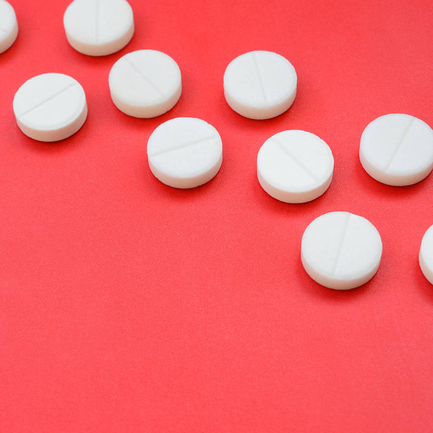 Alguns comprimidos brancos encontram-se sobre uma superfície de fundo vermelho brilhante. Imagem de fundo sobre tópicos médicos e farmacêuticos
 - Foto, Imagem