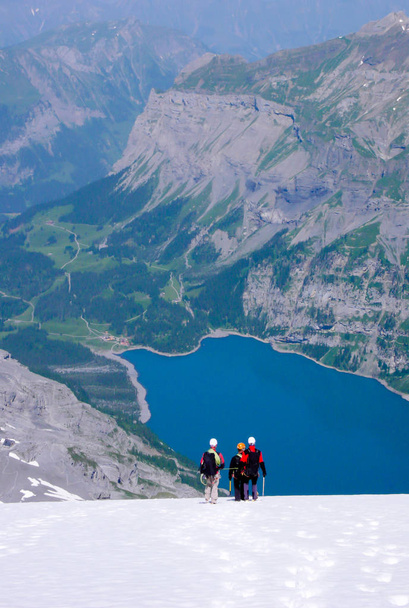 гірський гід з двома клієнтами вниз крутим білим льодовиком з фантастичним блакитним гірським озером далеко нижче
 - Фото, зображення