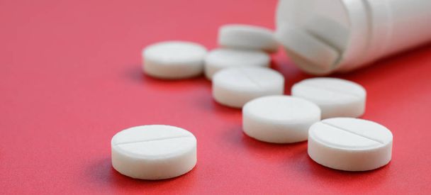 Vários comprimidos brancos caem do frasco de plástico na superfície vermelha. Imagem de fundo sobre tópicos médicos e farmacêuticos
 - Foto, Imagem