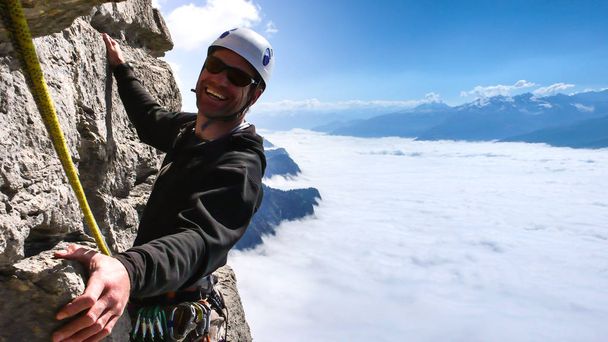 egy függőleges szikla mászás, gyönyörű környezetben, magasan a tenger a felhők a lenti völgyben mosolygó férfi túravezető - Fotó, kép