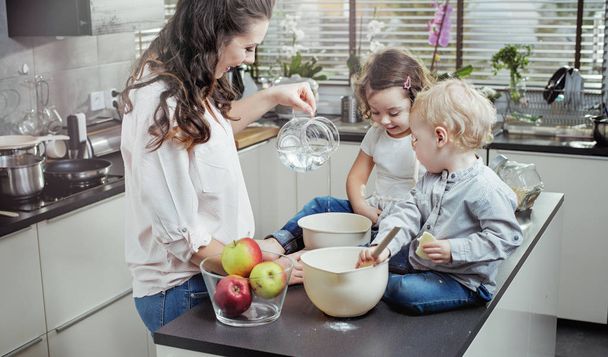 Cheerful mother teaching her children how to bake a cake - Фото, зображення