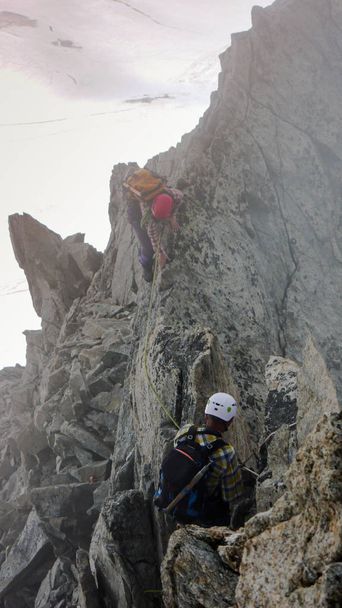 vuoristo-opas ja asiakas matkalla kohti korkeaa Alppien huippukokousta sumuisena päivänä
 - Valokuva, kuva