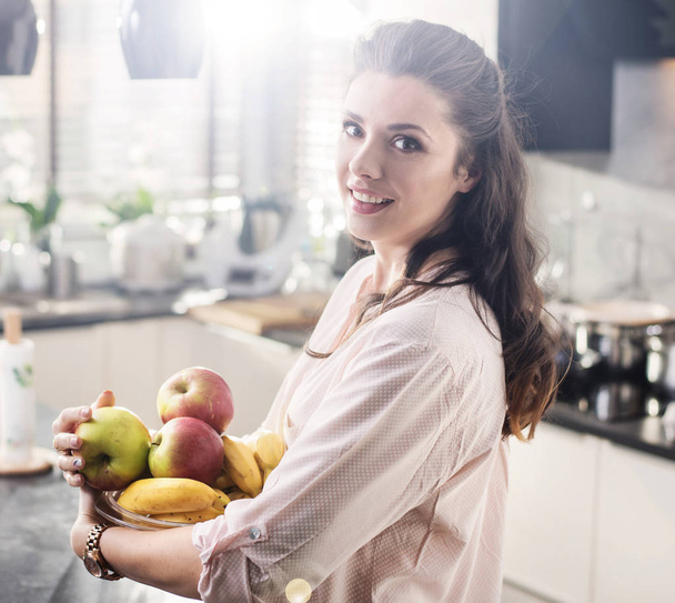 Cheerful woman holding a bowl full of fruit - Foto, afbeelding