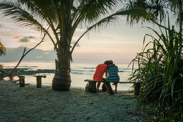 Egy fiatal pár ül a padon egy pálmafa alatt - Fotó, kép