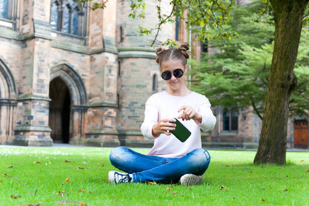 Young teenage girl with smartphone sitting in Glasgow University - Фото, изображение