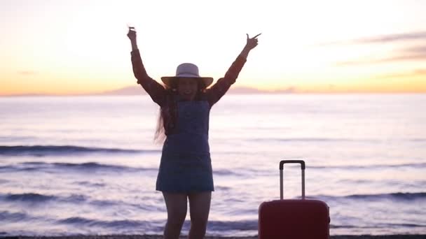 Ευτυχισμένη γυναίκα τουριστικά με βαλίτσα κοντά στη θάλασσα για το ηλιοβασίλεμα - Πλάνα, βίντεο
