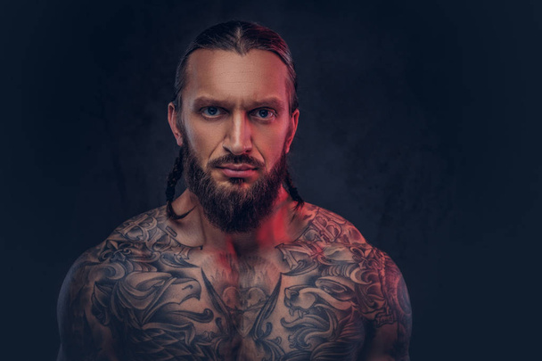 Portrait en gros plan d'un homme tatoué barbu musclé avec une coupe de cheveux élégante, isolé sur un fond sombre
. - Photo, image
