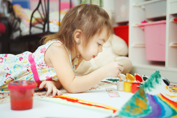 Маленька дівчинка лежить на підлозі спальні і малює картину
 - Фото, зображення