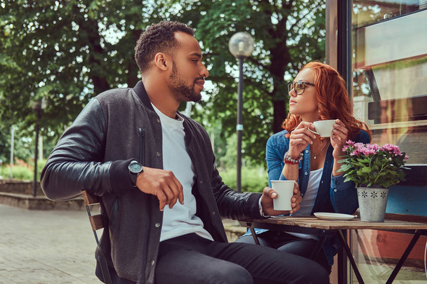Ένα ζευγάρι γνωριμίες πίνοντας καφέ, κάθονται κοντά στο κατάστημα καφέ. Σε εξωτερικούς χώρους σε μια ημερομηνία. - Φωτογραφία, εικόνα