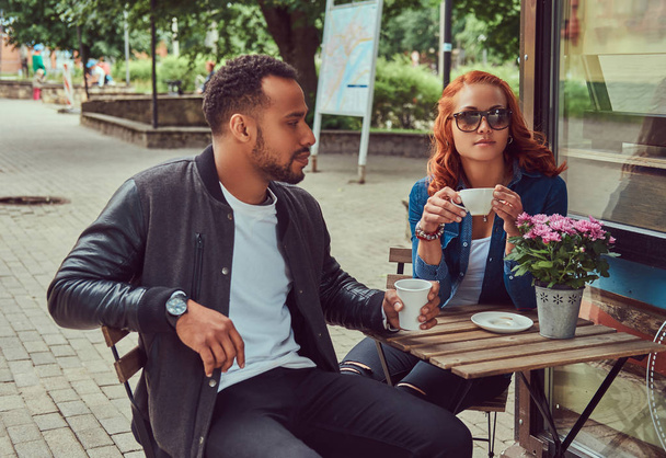 A couple dating drinking coffee, sitting near the coffee shop. Outdoors on a date. - Fotoğraf, Görsel