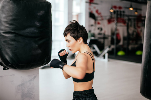 young woman is improving boxing skills with black huge boxing bag - Photo, Image
