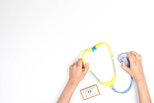 Draufsicht auf Kinderhände mit Spielzeug-Stethoskop auf weißem Hintergrund. - Foto, Bild