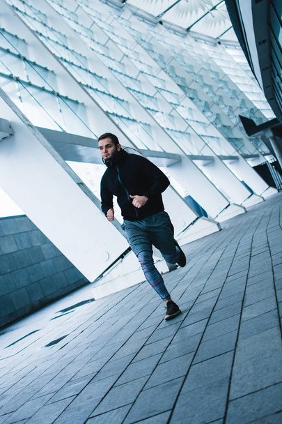 Snelheid in actie. Volledige lengte van de jongeman in sportkleding joggen tegen industriële Stadszicht - Foto, afbeelding