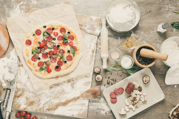 Top view cooking pizza. Ingredients, tomatoes, salami and mushrooms on wooden table - Foto, Bild