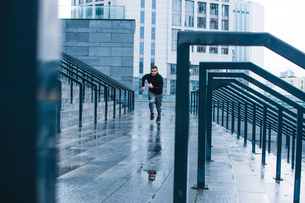 Швидше і сильніше. Повна довжина молодого чоловіка в спортивному одязі біжить по сходах проти промислового міста
 - Фото, зображення