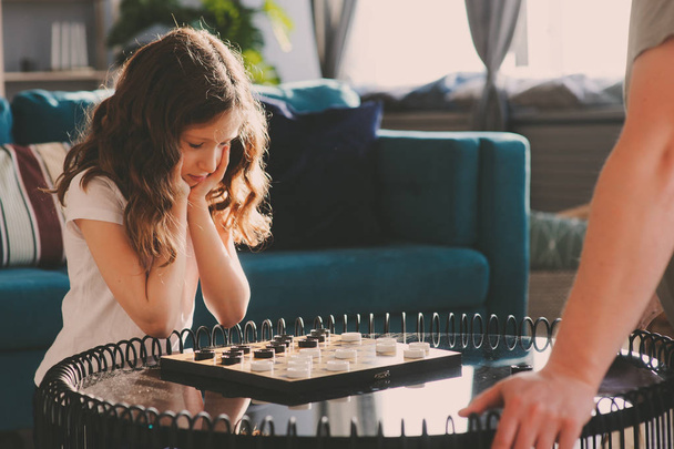 child girl playing checkers with her dad at home. Fatherhood and quality family time concept - Fotó, kép