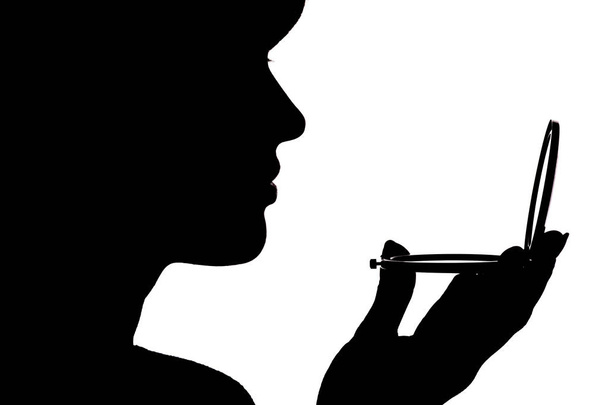 silhouette profile of a woman face looking in a pocket mirror, the concept of the beauty and fashion - Foto, immagini