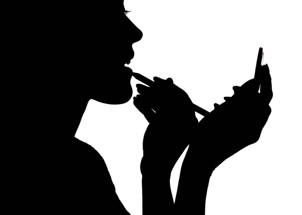 silhouette of woman doing make-up in front of pocket mirror in hands on white isolated background - Photo, Image
