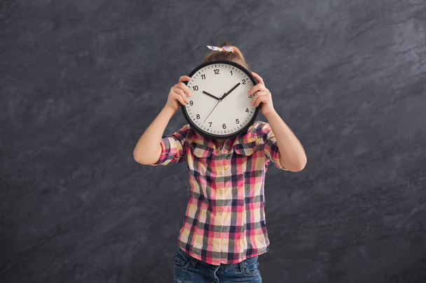 Menina segurando grande relógio, cobrindo seu rosto
 - Foto, Imagem