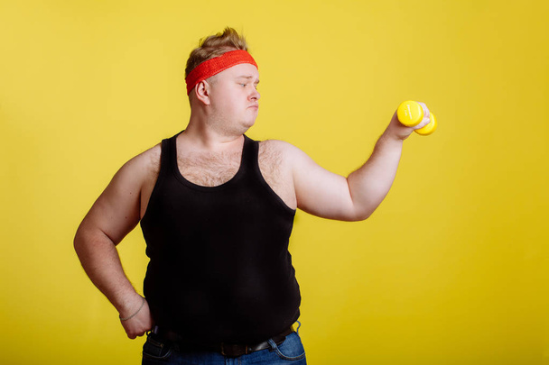 fat man with dumbbell on yellow background. Motivation for fat people - 写真・画像