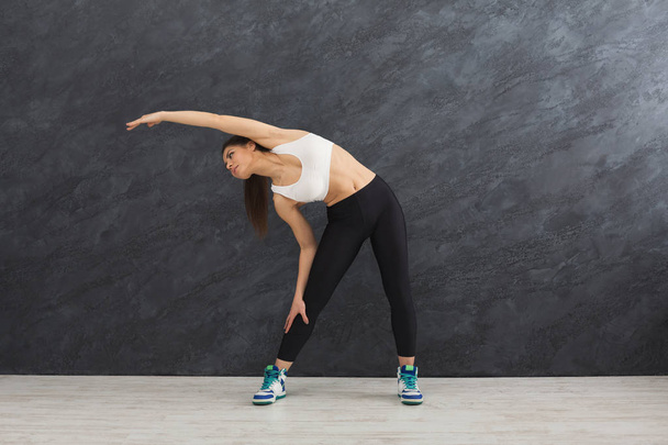 Fitness woman stretching at grey background indoors - Photo, Image