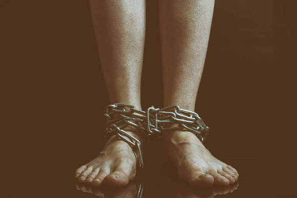Vuile vrouw voeten met gezwollen aderen hangen gebonden metalen kettingen close-up op een zwarte achtergrond, afgezwakt naar een retro film. - Foto, afbeelding
