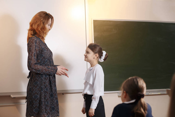 Foto des Lehrers, der Summe auf Tafel schreibt und hübsche Schülerin in der Nähe ansieht - Foto, Bild
