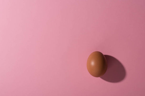 Minimalism. one egg in a corner with deep shadows on light pink background with copy space - Photo, Image