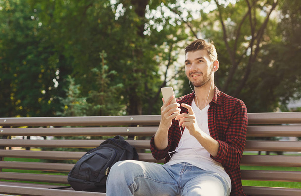 Happy νεαρό όμορφος άνδρας κάθεται σε εξωτερικούς χώρους και χρησιμοποιώντας το smartphone - Φωτογραφία, εικόνα