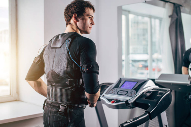 Man in black suit for ems training running on treadmill at gym - Фото, зображення