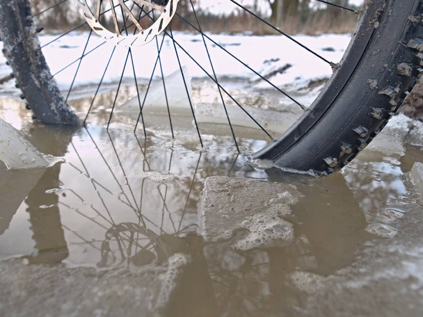 Велосипед утонул в грязном бассейне в зимней поездке. Разбитые куски льда вокруг замерзающей террановой шины
 - Фото, изображение