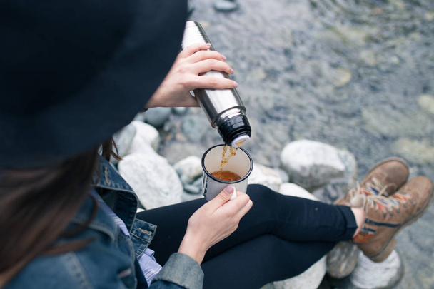 旅行者の女の子が魔法瓶カップ、屋外からお茶を注ぐします。若い女性のカップでお茶を飲みます。テーマ旅行。サーモスのマグで温かい飲み物を注いで、女。ハイキング中にお茶を飲む女の子 - 写真・画像